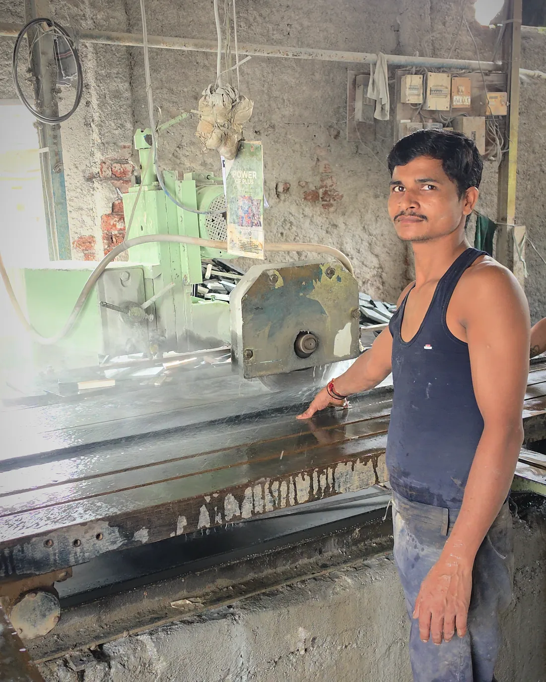 A worker standing beside the bridge saw at Ashish Marble & Granite, a cut slab on the bed in front of him.