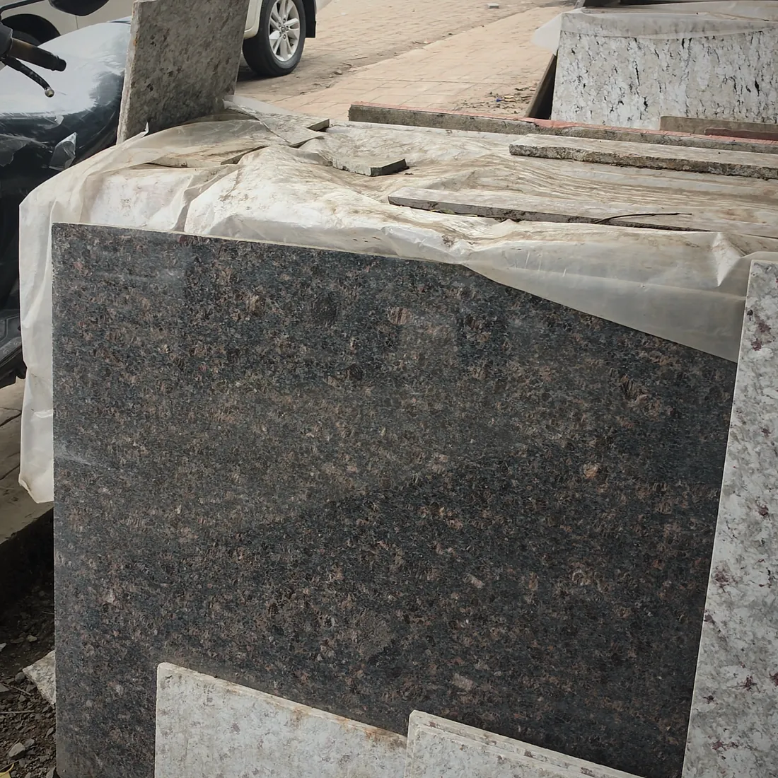 A dark speckled granite slab stacked against pale travertine-coloured stone in the yard.